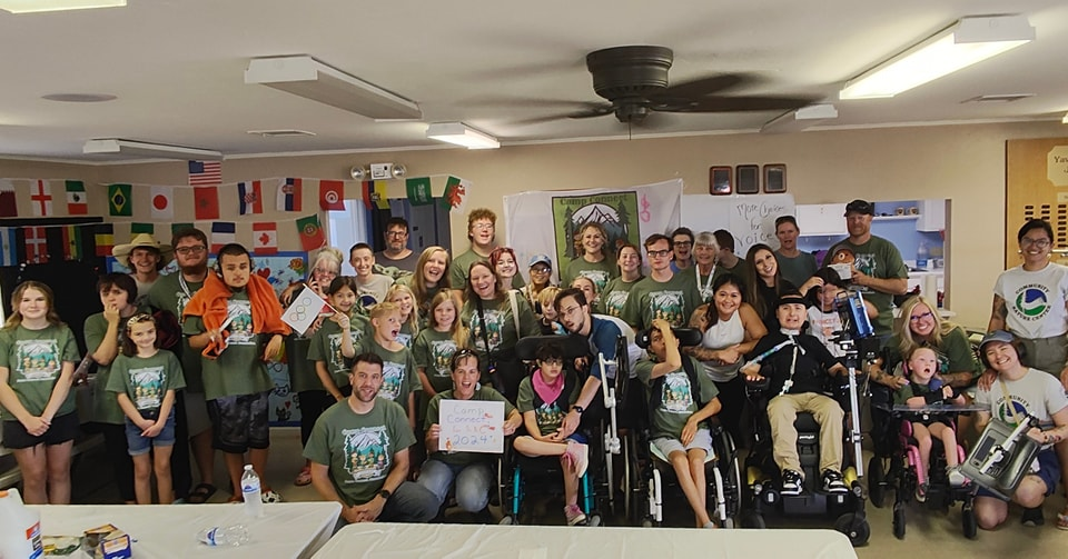 Image of a large group of AAC users and camp counselors all smiling together in a classroom.